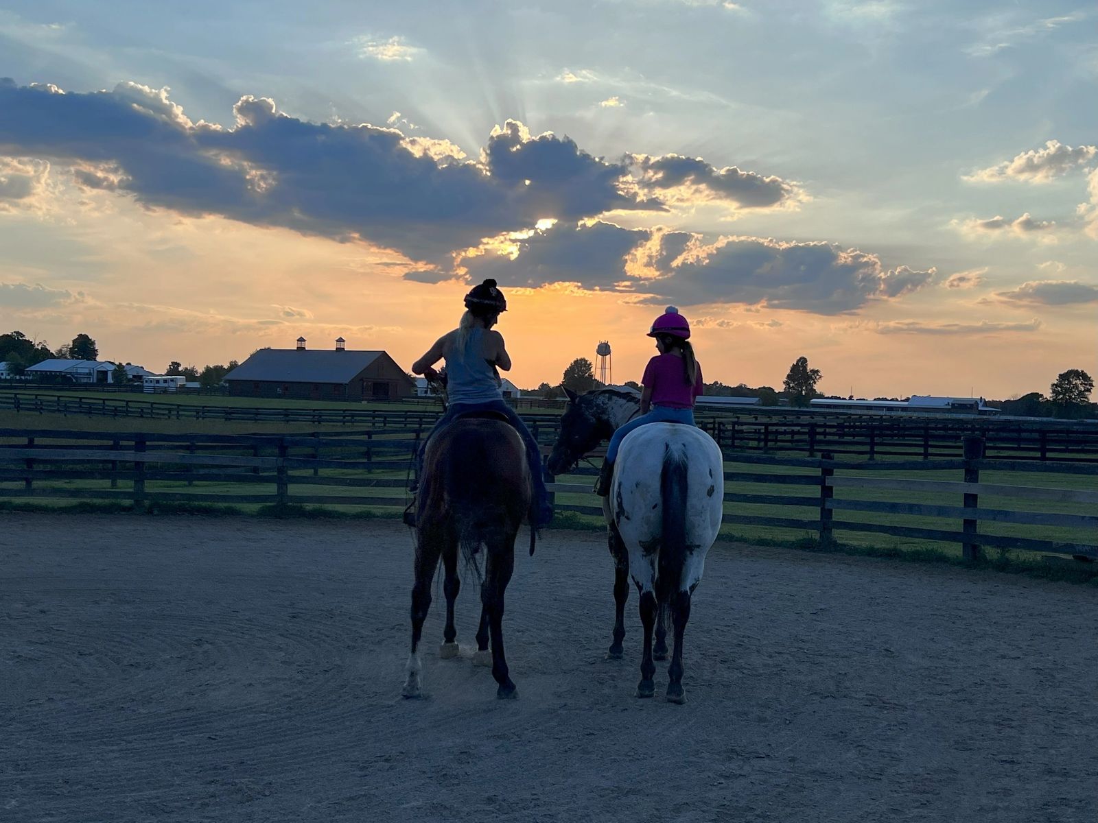 Two riders on horseback in the arena under a dramatic sunset sky